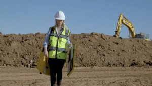woman walking on a construction site with an AeroPoint and AeroPoint backpack with a digger in the background