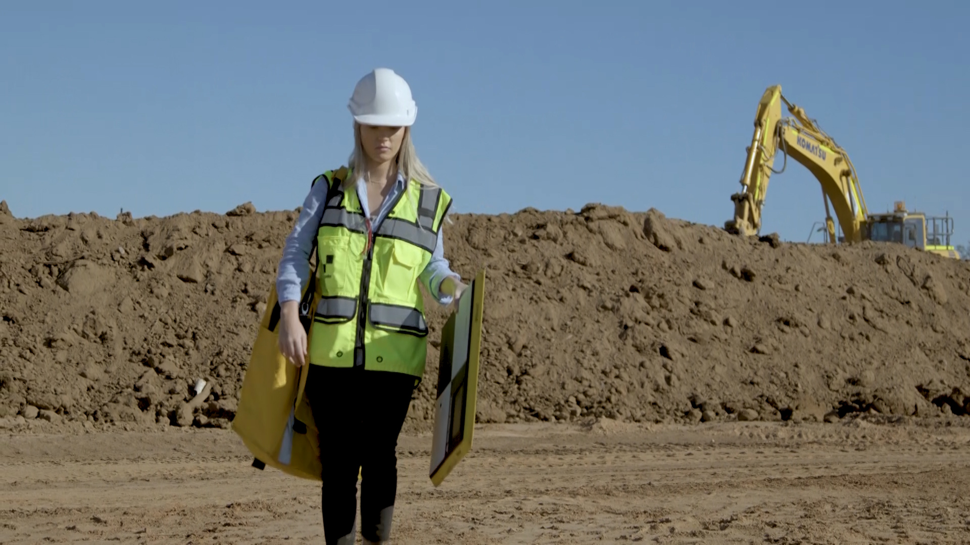 woman walking on a construction site with an AeroPoint and AeroPoint backpack with a digger in the background