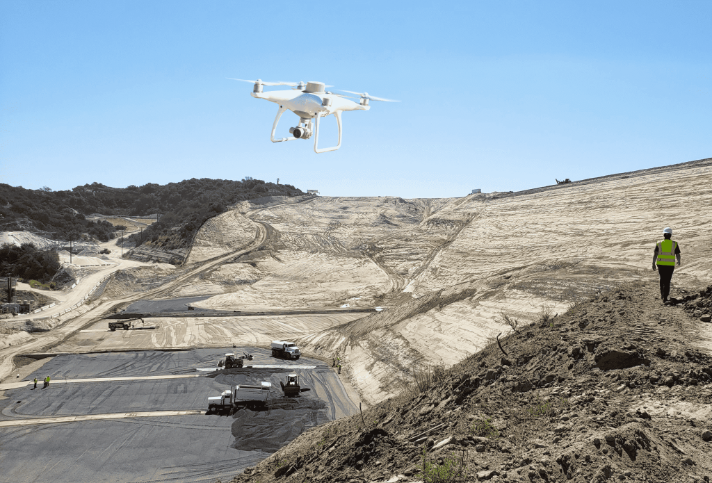 An aerial photo of a drone flyer over a waste management site, with the pilot in the background.