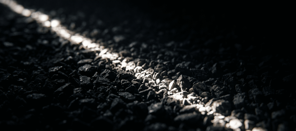 A thin line of light raking across dark crushed aggregate, revealing its surface texture
