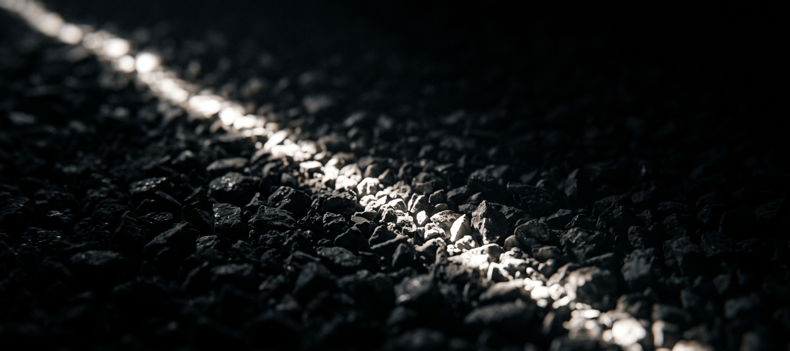 A thin line of light raking across dark crushed aggregate, revealing its surface texture