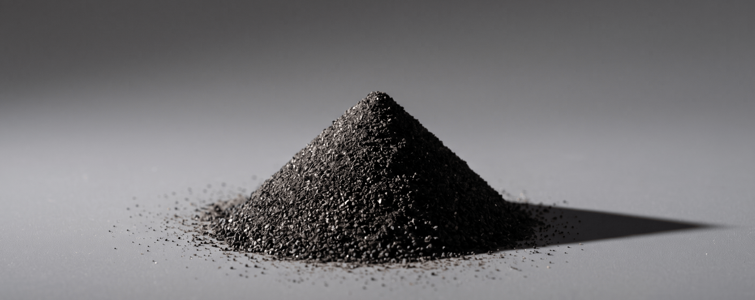 A small perfect cone of dark aggregate lit from the side against a neutral background